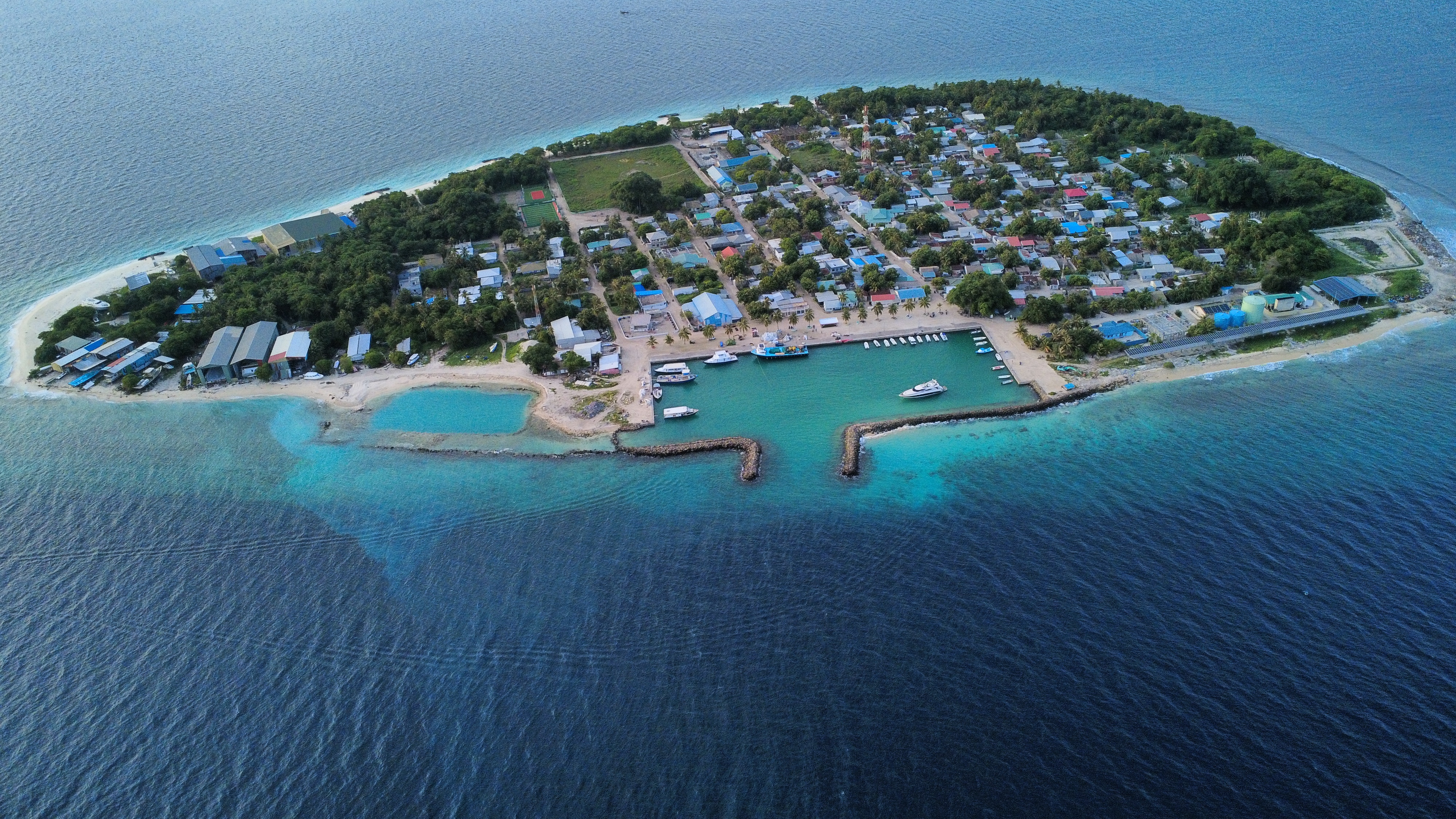 Aerial view of Innamaadhoo island, harbor, turquoise lagoon, and surrounding reef